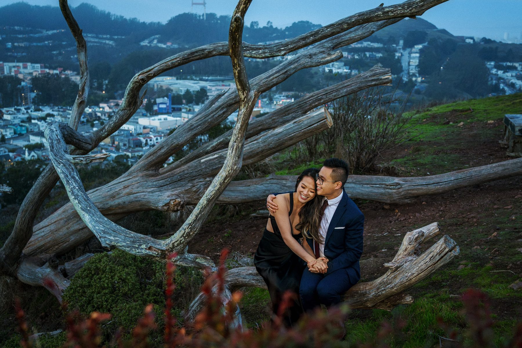 Engaged couple seated on a scenic hillside overlooking San Francisco