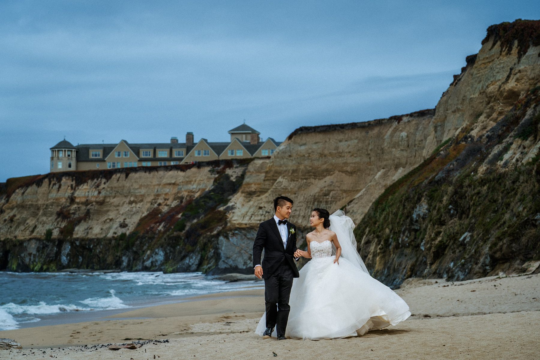 Bride and groom walking on the beach beneath The Ritz-Carlton, Half Moon Bay